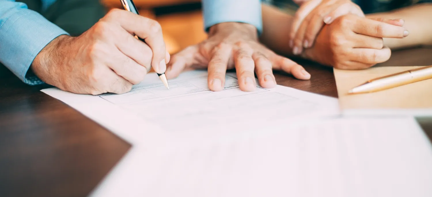 Two people reviewing and signing a business contract at a desk